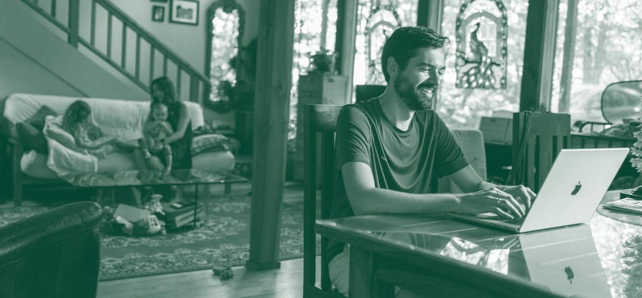 Man sitting at a laptop in a house with children behind him